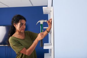 woman using a hammer to mount a floating shelf